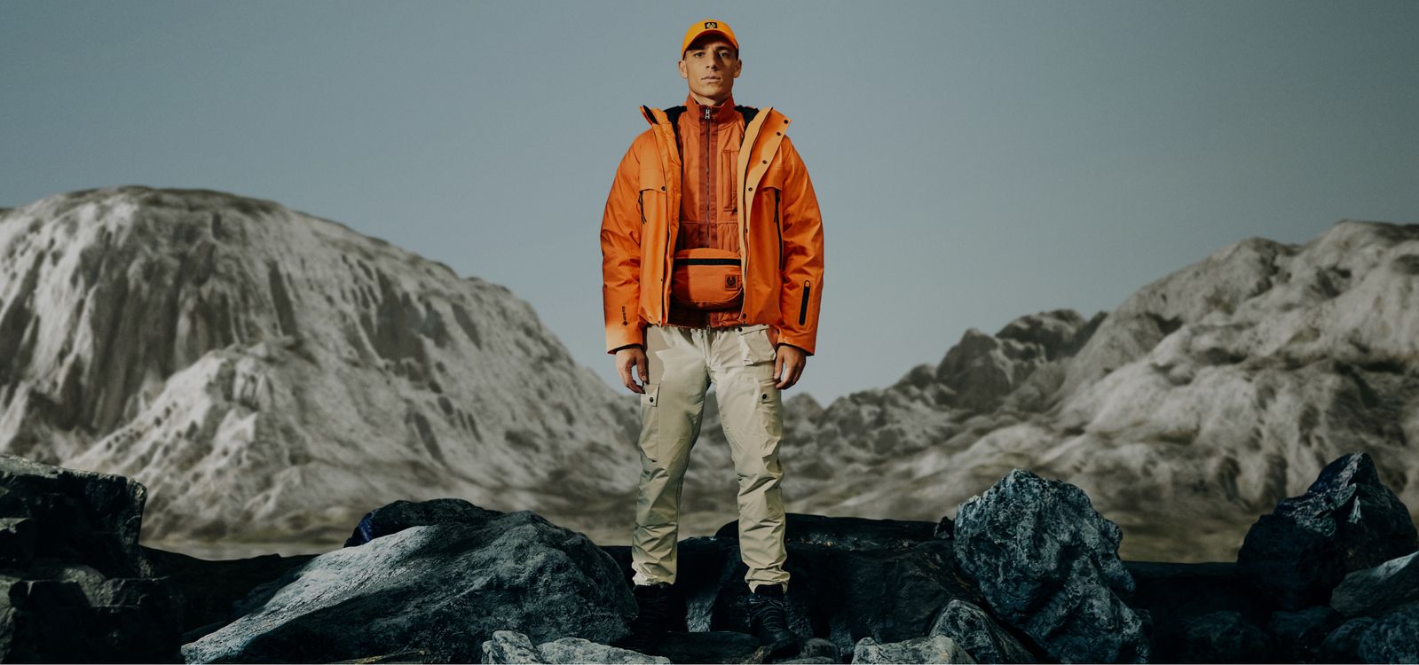 Male model is wearing the Astral Jacket in Signal Orange, the Sector Overshirt in Amber and the Trialmaster Cargos in Fawn.